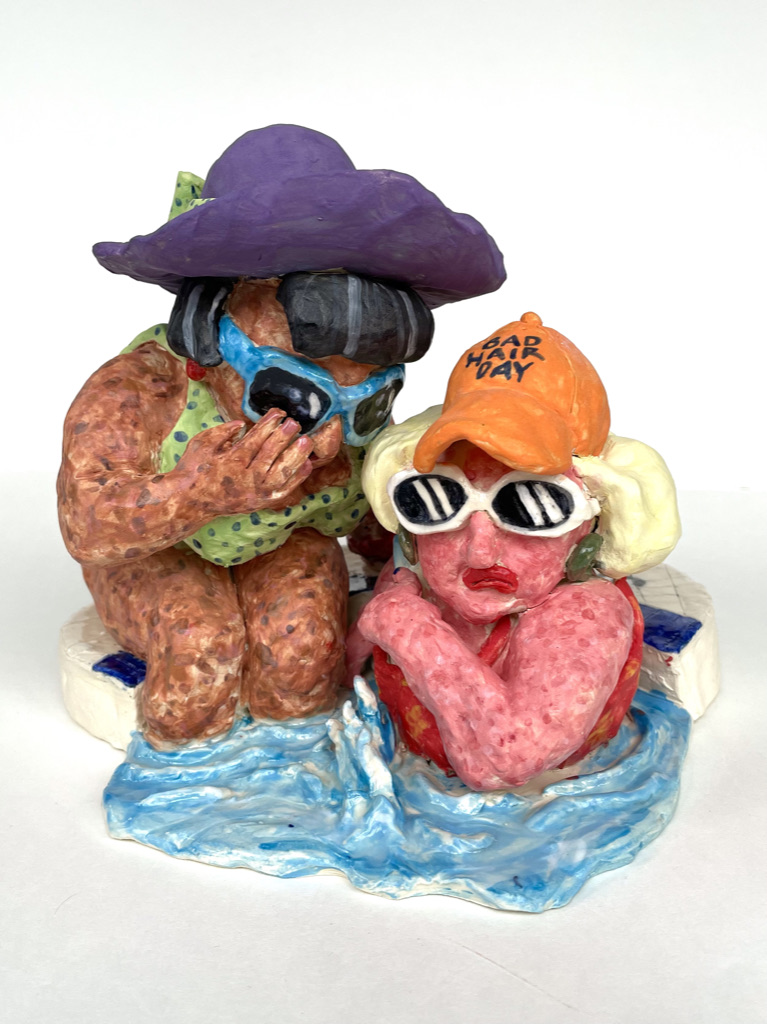 A sculpture of two women in bathing suits whispering to each other